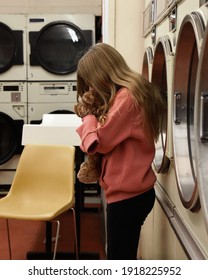 A Child Is Standing In A Laundromat Holding A Teddy Bear And Looks Worried Or Sad For A Childhood Responsibility Concept About Clean Clothes.