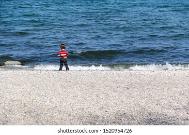 Child standing on rocky shore in front of rough sea and amazed by the scene