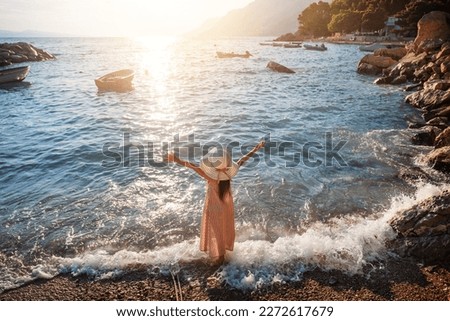 Child is standing on sea beach among waves, raising his hands to sun. Hello summer, wonderful sea vacation concept.