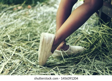 Child Is Standing On A Tip Toe Feet On The Green Grass In A White Sneakers