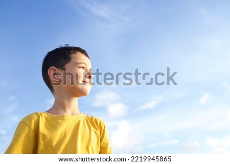 Child standing in profile blue sky with clouds on background. Boy 8 years old brunette, smiling face. Kid in yellow T-shirt. Concept of children, growing up, peace, look, dreams, children. Sunny day.