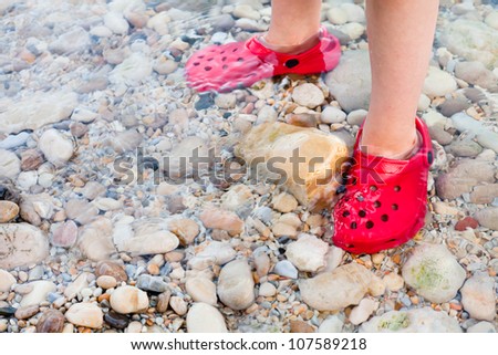 Child standing in shallow water with nice red shoes