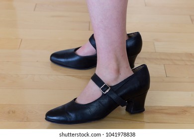 Child Standing Wearing Adult Black High Heeled Shoes Too Big For Her, Against Hardwood Floor