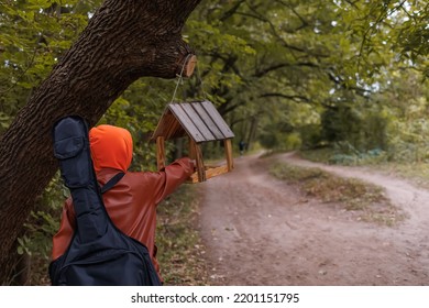 The Child Stands With His Back And Pours Food Into The Bird Feeder