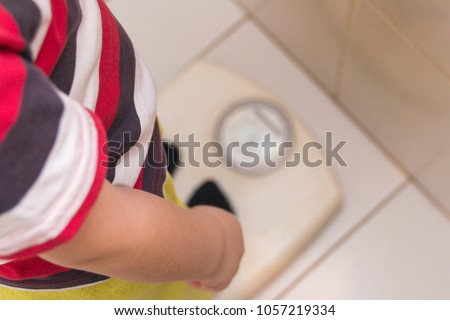 The child stands on the floor scales in a striped T-shirt, the view from the top. Health