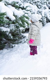 child stands in a snowdrift near the Christmas trees and shakes the snow from the branches of trees. Winter games for children with snow. Happy child in a snowdrift