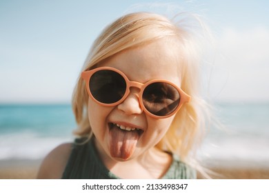 Child sticking out tongue emotional girl in sunglasses 3 years old baby walking on beach family travel lifestyle vacations holidays