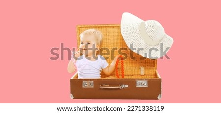 Child with straw summer hat sitting in suitcase on pink background