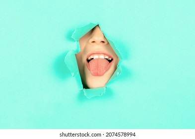 Child Stuck Out Her Tongue Through A Hole In The Paper. Boy Shows His Tongue Through Hole In The Wall. Portrait Funny Kid Man Showing Tongue In A Torn Paper Hole.