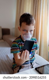 The Child Suffers From Bronchitis, Undergoes Inhalation Treatment At Home. Photo Of A Unhealthy Young Boy Wearing Oxygen Mask At Home While Using Mobile. Health, Medical Equipment And People Concept.