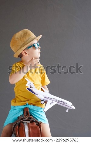 A child in summer clothes and sunglasses sits on a suitcase and holds a toy airplane in his hands. Waiting for travel. Family vacation. Dreams of travel. Summer vacation
