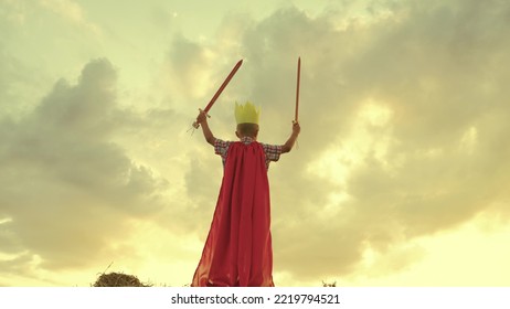 Child Superhero Game Sunset. Red Cape Childish Fantasy. Countryside. Golden Crown Head Kid. Achieve Victory Success. Schoolboy Plays Sword. Happy Child Superman Red Raincoat Nature. Concept Happy