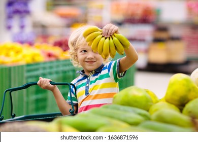Child in supermarket buying fruit and juice. Kid grocery shopping. Little boy with cart choosing fresh vegetables in local store.