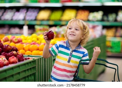 Child In Supermarket Buying Fruit And Juice. Kid Grocery Shopping. Little Boy With Cart Choosing Fresh Vegetables In Local Store.