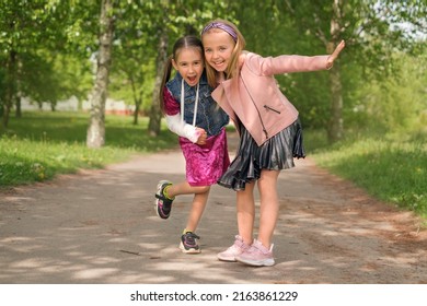 Child Supports His Best Friend With A Broken Arm With Cast On Forearm.  Two Little Girls Of Preschool Age Are Hugging And Laughing And Shouting Merrily. Happy Childhood. Small Fashionistas In Dresses