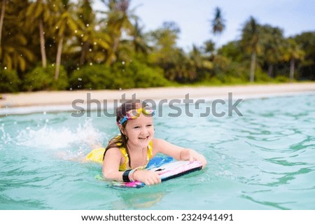 Child surfing on tropical beach. Family summer vacation in Asia. Kids swim in ocean water. Kid on surf body board. Little child swimming in exotic sea. Travel with children. Water and beach sport.
