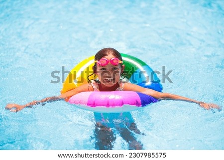 Child in swimming pool floating on toy ring. Kids swim. Colorful rainbow float for young kids. Little girl having fun on family summer vacation in tropical resort. Beach and water toys. Sun protection