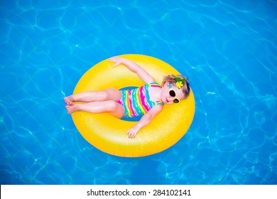 Child In Swimming Pool. Little Girl Playing In Water. Vacation And Traveling With Kids. Children Play Outdoors In Summer. Kid With Inflatable Ring Toy. Swim Wear And Sun Glasses For UV Protection.