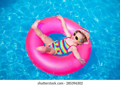 Child In Swimming Pool. Little Girl Playing In Water. Vacation And Traveling With Kids. Children Play Outdoors In Summer. Kid With Inflatable Ring Toy. Swim Wear And Sun Glasses For UV Protection.