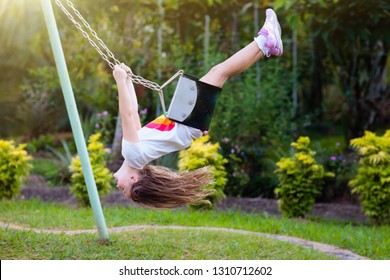 Child swinging on playground on sunny summer day in a park. Kids swing. School or kindergarten yard and play ground. Little girl flying high in the air on swing. Summer outdoor activity. Kid playing.