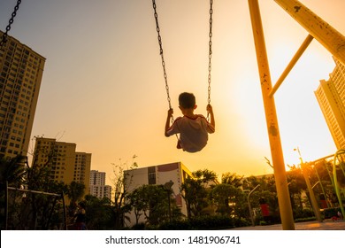 Child swinging on swing in sunset in city with building on background