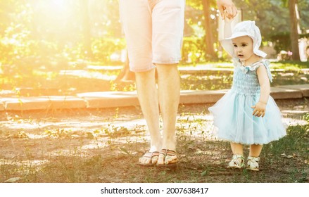 The child takes the first steps with the help of the father outdoor. the parent holds the hand of a small child on nature. Space for text