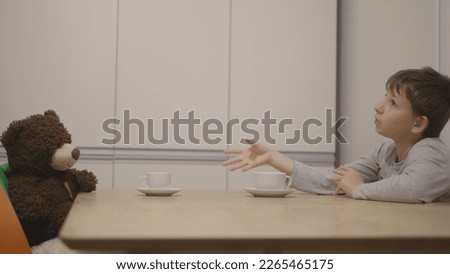 Child talk and drink tea with teddy bear , sit with imaginary friend at table