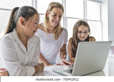 A Child With Technology Tablet And Laptop Computer In Classroom Teacher On The Background