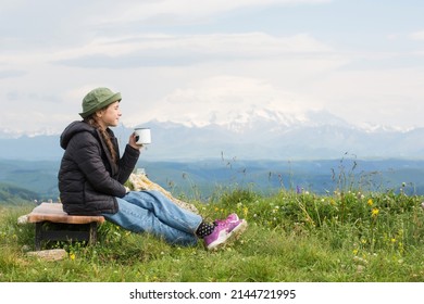 child teen sits against backdrop of mountains and drinks tea from cup in hike. travel, hiking, journey, outdoor recreation - Shutterstock ID 2144721995