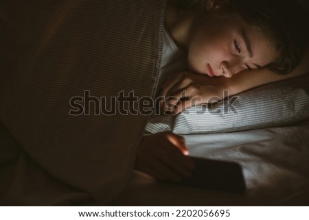 child teenager girl lies in bed in evening or at night and looks into phone. mobile addiction