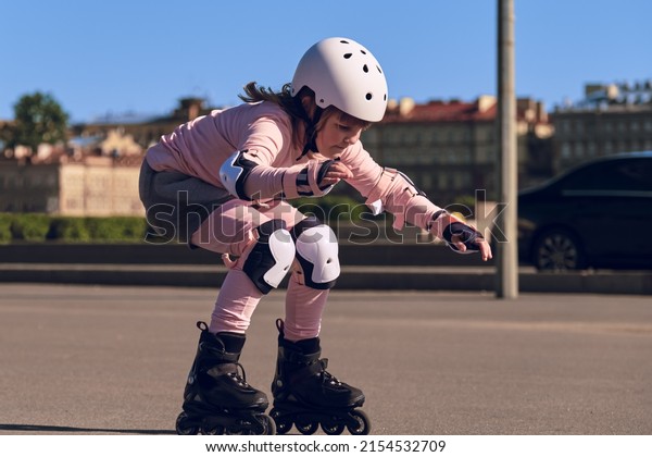 A child of ten is\
learning to ride rollerblades on city streets. The girl is wearing\
fall protection. Roller skating on the road. Young sportswoman\
doing sports outdoors .