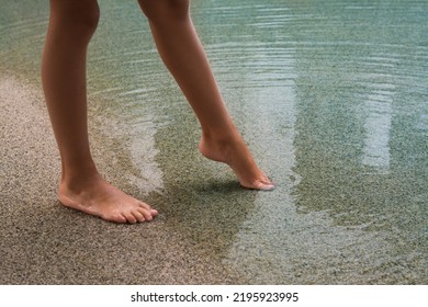 Child Testing Sea Water Temperature With Foot On Beach, Closeup