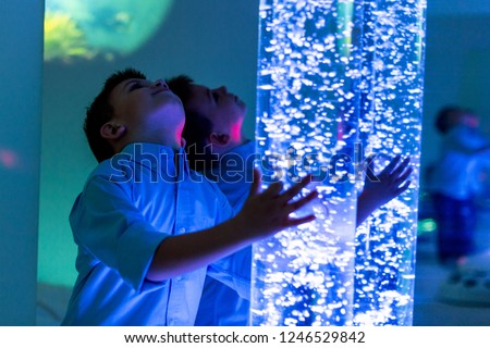 Child in therapy sensory stimulating room, snoezelen. Child interacting with colored lights bubble tube lamp during therapy session.