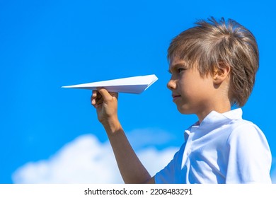 Child Throwing White Paper Plane. Boy Playing With Paper Airplane Against Blue Sky On Sunny Day Outdoors