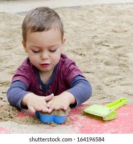 Child Toddler, Boy Or Girl, Playing In Sandpit With Plastic Toys.