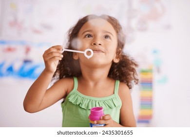 Child, toy and blowing bubbles for development, playing and having fun alone in home. Happiness, bokeh and face of young girl in bedroom for entertainment, soap bubble wand and activity games - Powered by Shutterstock
