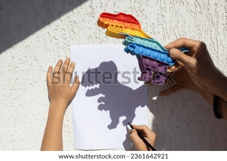 child traces a contrasting shadow from a dinosaur on paper on a sunny day. happy cheerful childhood, ideas for games, lifestyle, development of imagination, creative games