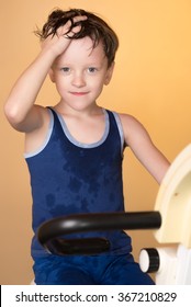 The child is trained on a stationary bike . Leads a healthy lifestyle. The boy develops muscles . Tired and sweaty . Sport generation.