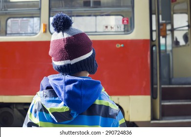 Child At Tram Or Bus Stop Waiting Door To Open, Tram With Open Door In The Background, Back View.