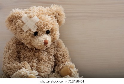 Child Trauma Concept.Teddy Bear With Bandage On Head Sitting On A Wooden Background. Copy Space