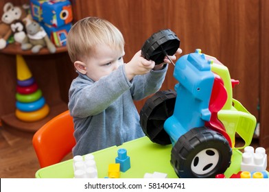 Child Tries To Fix A Broken Toy Tractor Indoor.