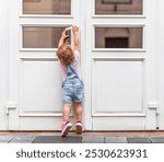 The child tries to open the door. The child reaches for the doorknob on the street.