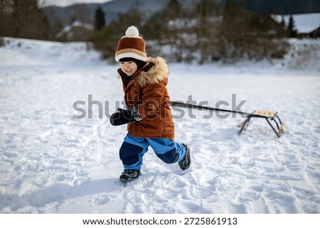 Child tries to pull a sled through the snow during a winter walk