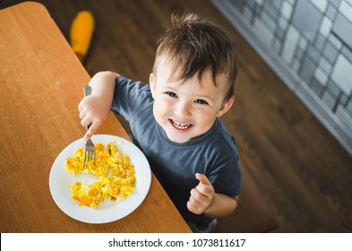 a child in a t-shirt in the kitchen eating an omelet, a fork - Powered by Shutterstock