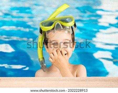 Child with tuba mask and snorkel with hand on his nose smiling and happy.Happiness concept.Snorkeling, swimming, vacation concept in a home or hotel pool