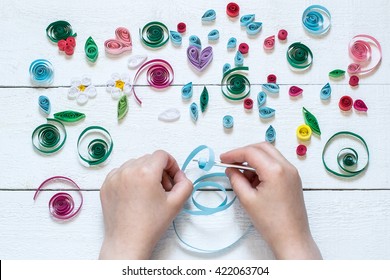 The child twists blanks for quilling. Many details of quilling laid on a white wooden table