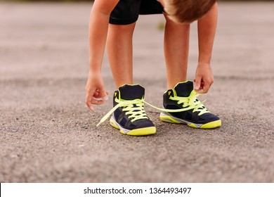 Child Tying Shoelaces On Sports Shoes In Summer Outdoors