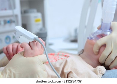 Child Is Under General Anesthesia. Surgery Under Anesthesia. Operating Room .Oxygen Mask On The Child's Face.Measurement Of Oxygen Levels In The Blood. A Child's Hand.Face Is Out Of Focus.