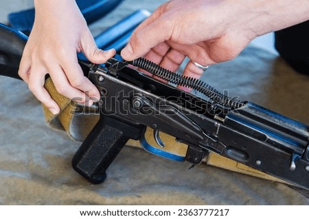 A child, under the guidance of an instructor, assembles a combat machine gun. Teaching children military affairs and preparing future soldiers. Close-up. Unrecognizable man