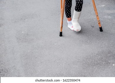 Child Using Crutches And Broken Legs For Walking Outdoor,Close Up. Broken Leg, Wooden Crutches, Ankle Injury. Bone Fracture And Ankle Fracture Bei Children. Patient Using Crutches For Walking Outdoor